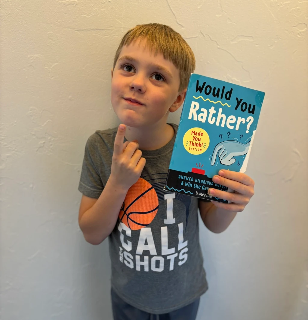 A boy holding a book called 'Would You Rather'