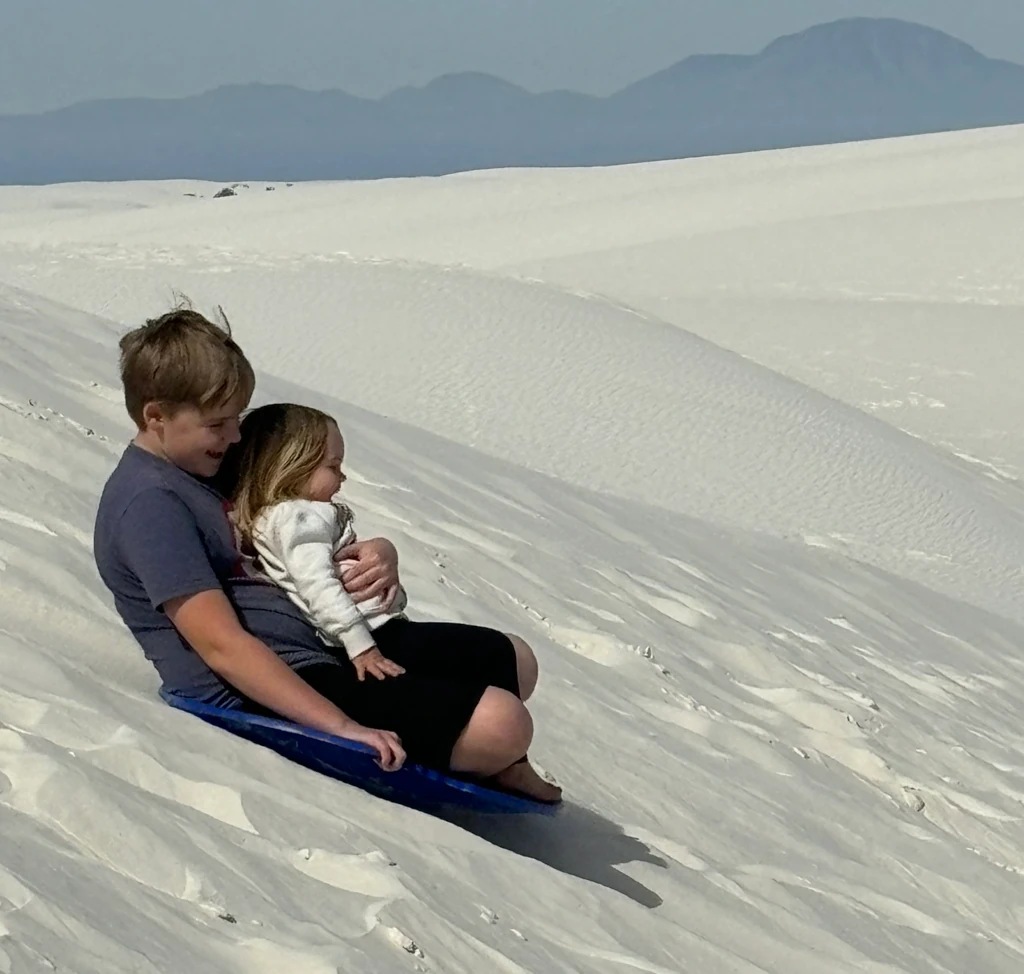 Two kids riding a sled down a sand dune