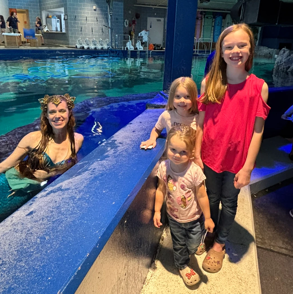 Three girls posing with a mermaid