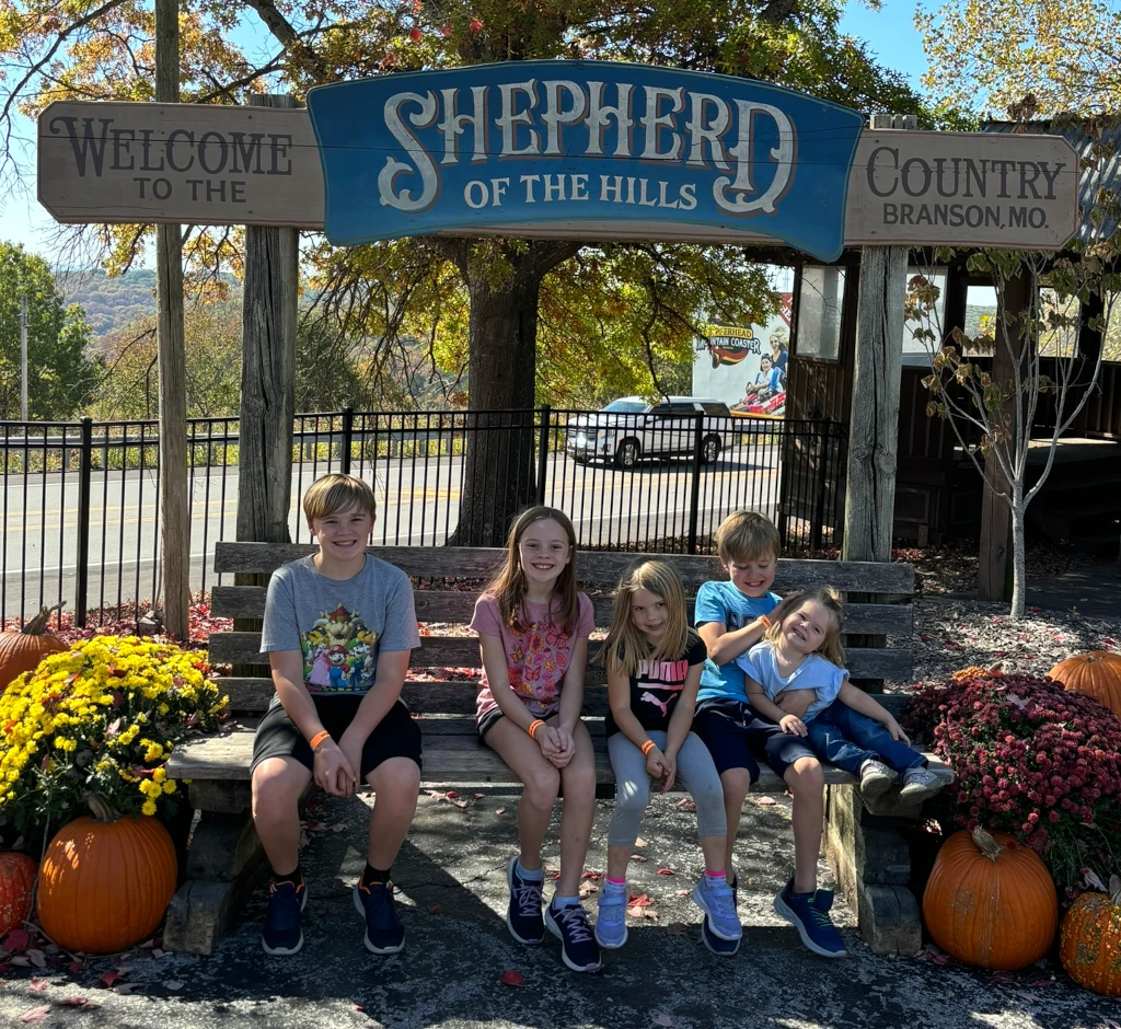 Kids sitting in front of a sign that says 'Shepherd of the Hills'