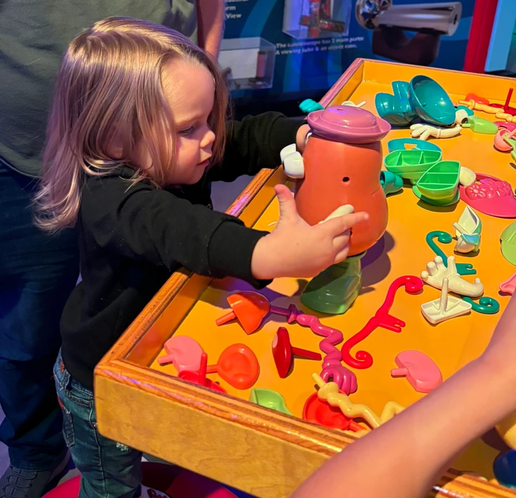 A little girl playing with a Mr Potato head toy