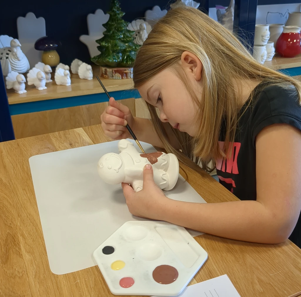 A little girl painting a piece of pottery