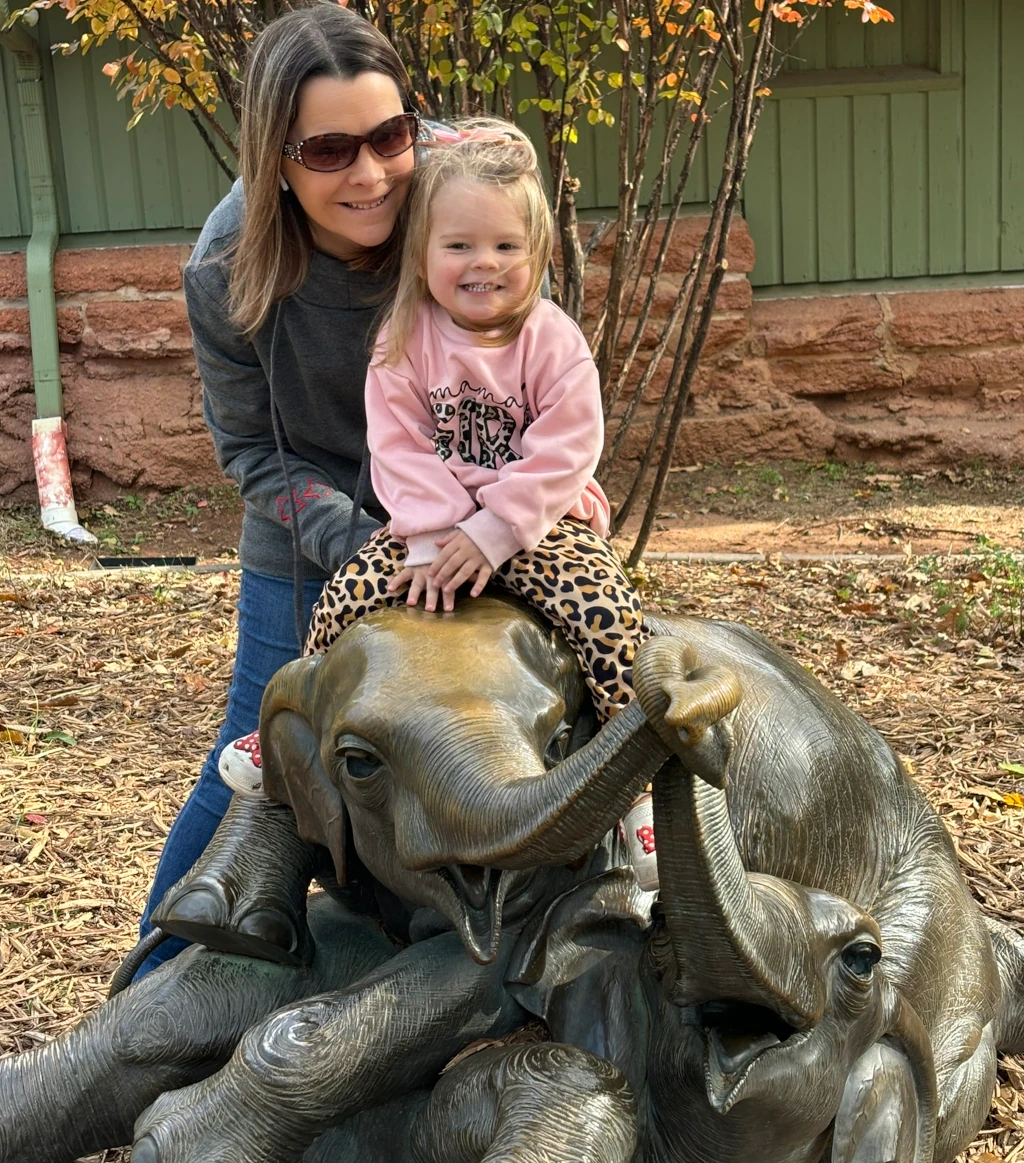 A little girl and her mom posing by an elephant statue