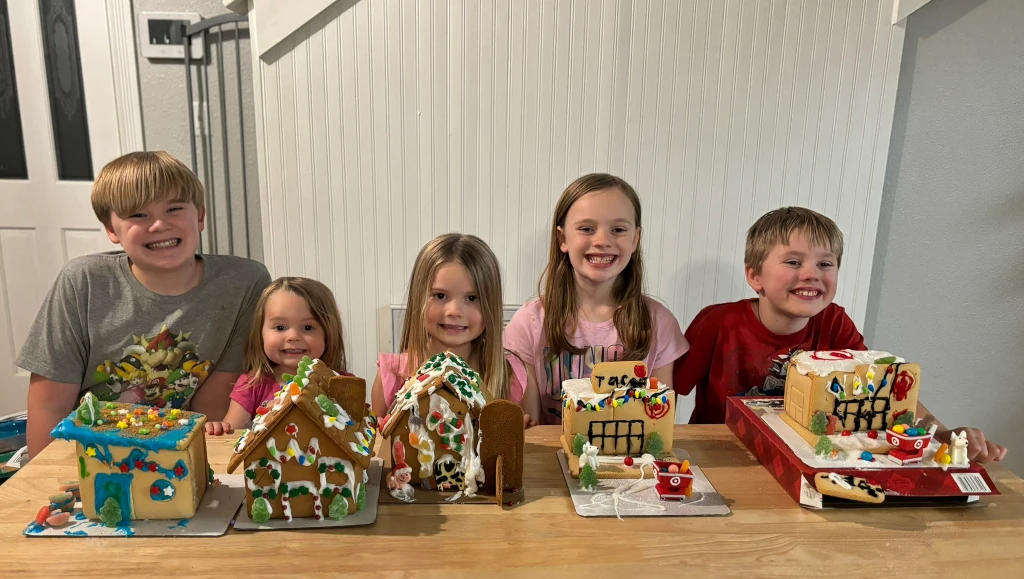 Kids sitting behind gingerbread houses that they made