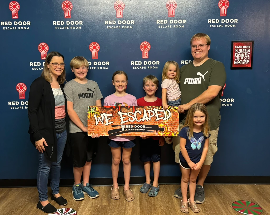 A family holding a sign that says 'Red Door Escape Room'