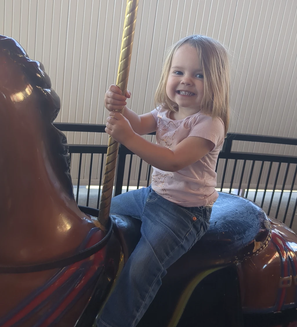 A little girl holding on to a carousel horse