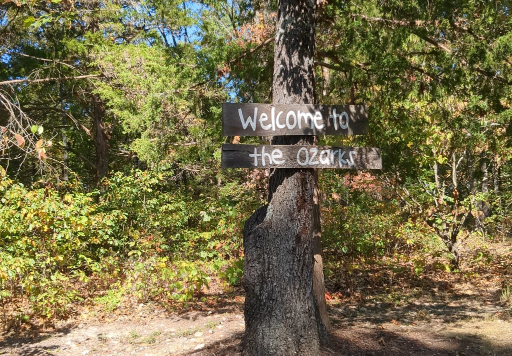 A sign hanging on a tree that says "Welcome to the Ozarks"